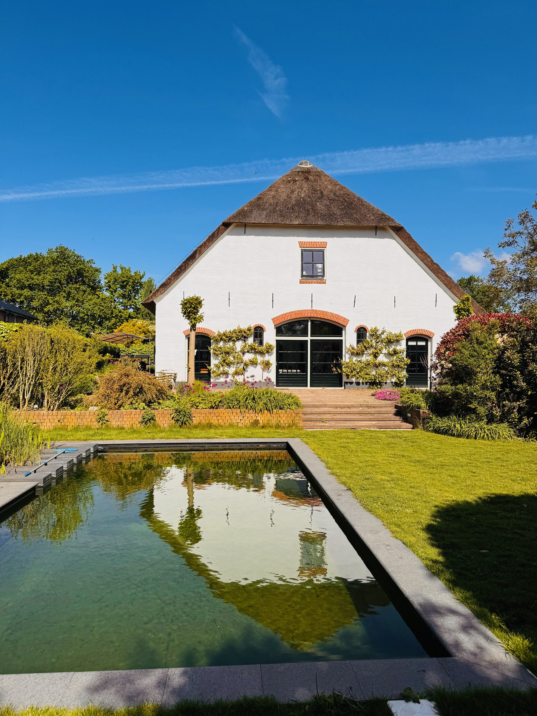 Grote spiegelvijver in de tuin met de rietgedekte boerderij weerspiegeld